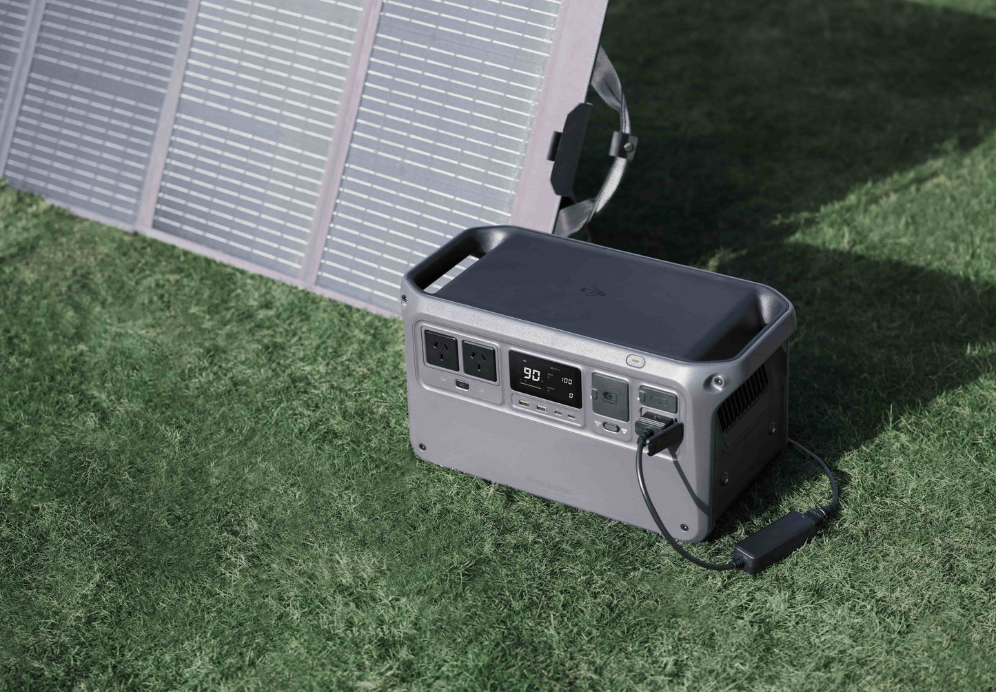 DJI Power 1000 charging via 120W solar panel on grass — portable off-grid power setup using DJI Power Car Outlet to SDC Power Cable; ideal for tradies, campers, and remote worksites, available from Yakka Gear.
