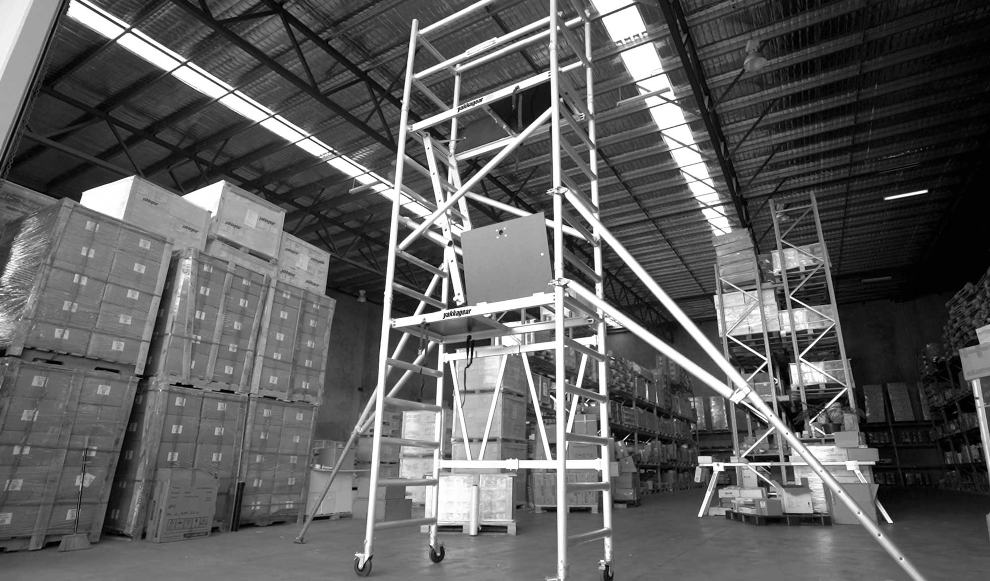 Yakka Gear Australia compact scaffolding tower as access equipment, including the Base Unit, Extension Unit, Tower Unit, and Adjustable Wheels. 1.44m Length x 0.74m Width, with working platform height of 3.9m and reach up to 6m high. View from the front side angle set up in the warehouse.