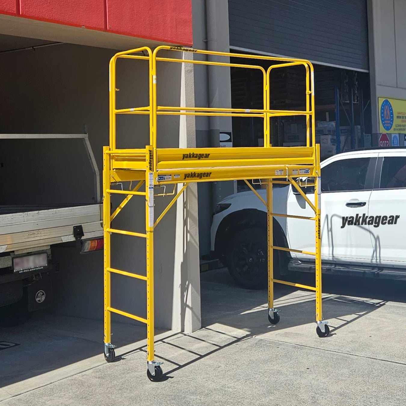 Rapid Mobile Scaffold complete system by Yakka Gear Australia pictured in warehouse, 3.8m reach with guard rails extended to maximum height, 1.87m L x 0.73m W platform, 1.81m adjustable platform height, heavy-duty powder-coated steel frame and lockable castor wheels.